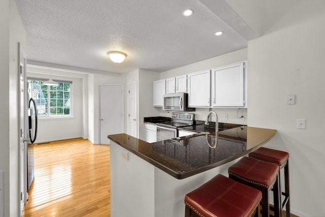 12 Southbridge Ct Unit 12, Simsbury, CT 06070 - kitchen featuring stainless steel appliances, a peninsula, a breakfast bar, dark stone countertops, and a textured ceiling