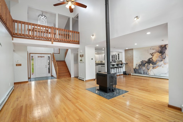 210 Founders Way, Stratford, CT 06614 - living room featuring a baseboard heating unit, light wood-style flooring, a towering ceiling, ceiling fan, and a wood stove