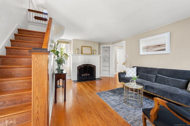 living area with a fireplace, light wood-style flooring, built in features, and stairs