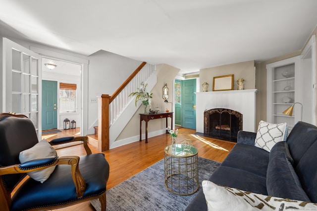 living area with wood finished floors, a fireplace, built in features, and stairway