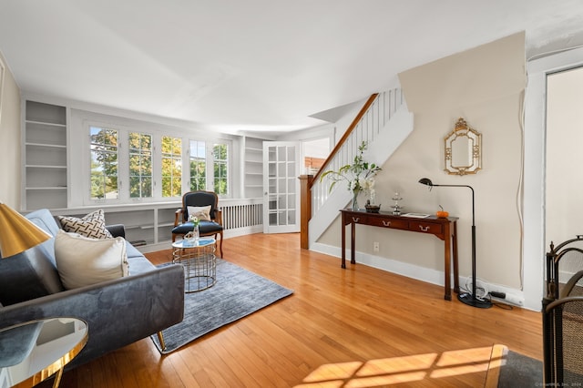 living room featuring built in shelves, baseboards, stairs, and light wood finished floors