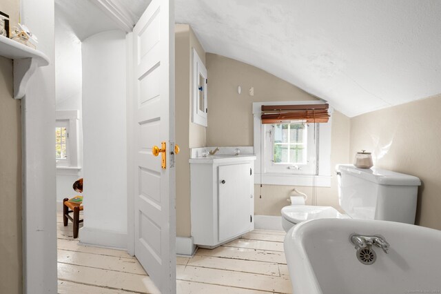 full bathroom featuring wood-type flooring, vaulted ceiling, a freestanding tub, and toilet