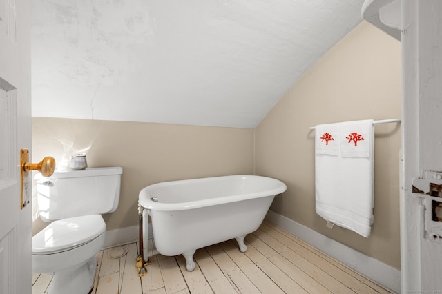 bathroom with vaulted ceiling, a soaking tub, toilet, and baseboards