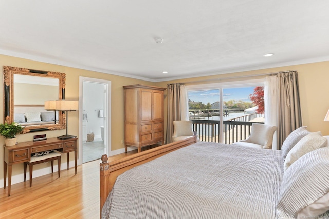 bedroom with crown molding, light wood-style flooring, a water view, and access to exterior