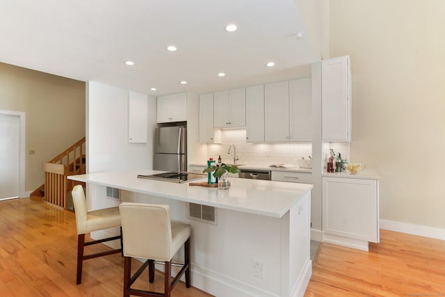 kitchen with white cabinets, light wood-style flooring, stainless steel appliances, decorative backsplash, and a kitchen bar