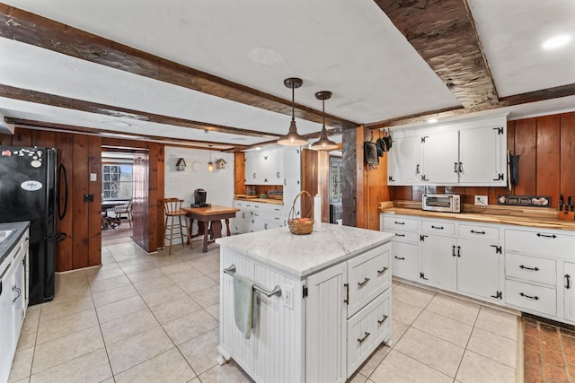 kitchen featuring light tile patterned flooring, wooden walls, decorative light fixtures, white cabinets, and freestanding refrigerator