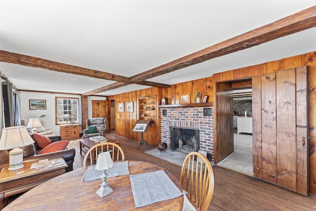 dining area featuring wood-type flooring, wood walls, beamed ceiling, and a fireplace
