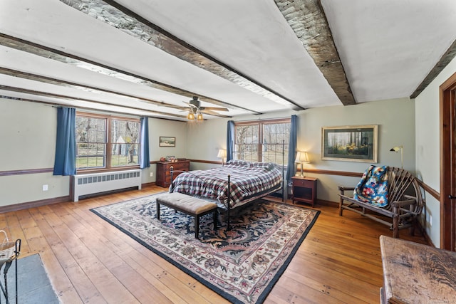 bedroom with radiator, hardwood / wood-style flooring, beamed ceiling, and multiple windows