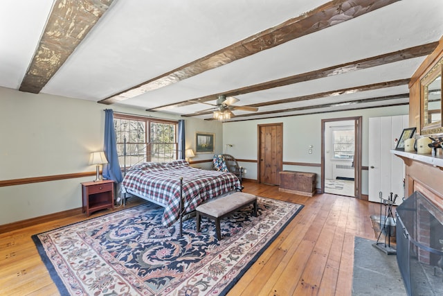bedroom featuring baseboards, a brick fireplace, hardwood / wood-style floors, and beamed ceiling