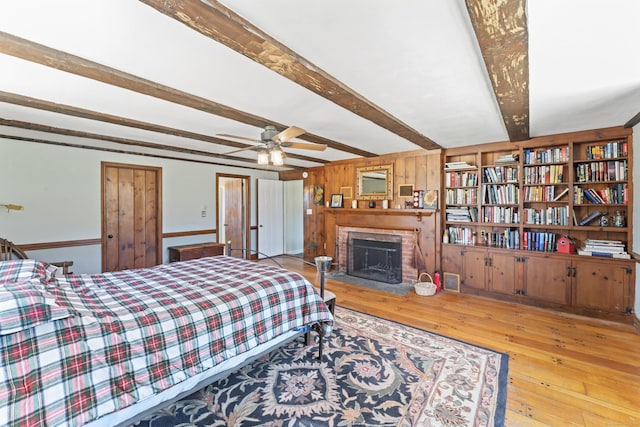 bedroom with a brick fireplace, beam ceiling, and hardwood / wood-style floors
