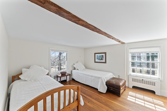bedroom featuring radiator heating unit, wood finished floors, and beam ceiling