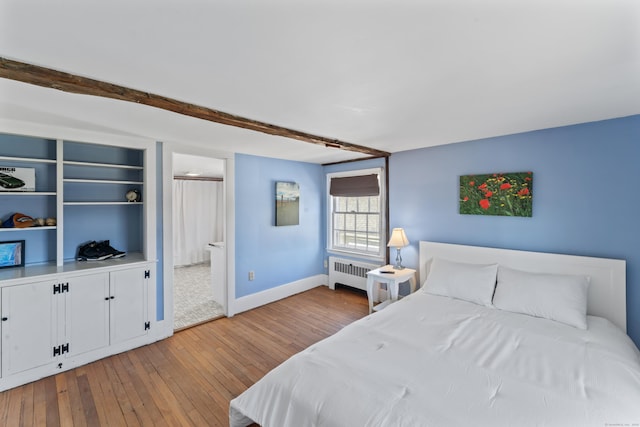 bedroom with hardwood / wood-style flooring, connected bathroom, radiator, baseboards, and beam ceiling
