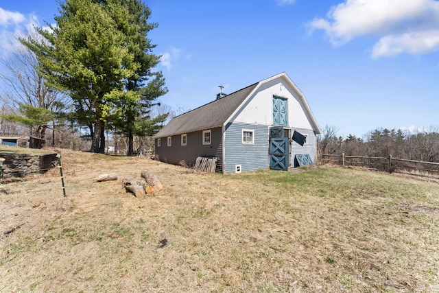 view of property exterior featuring a gambrel roof, a barn, fence, an outbuilding, and a lawn
