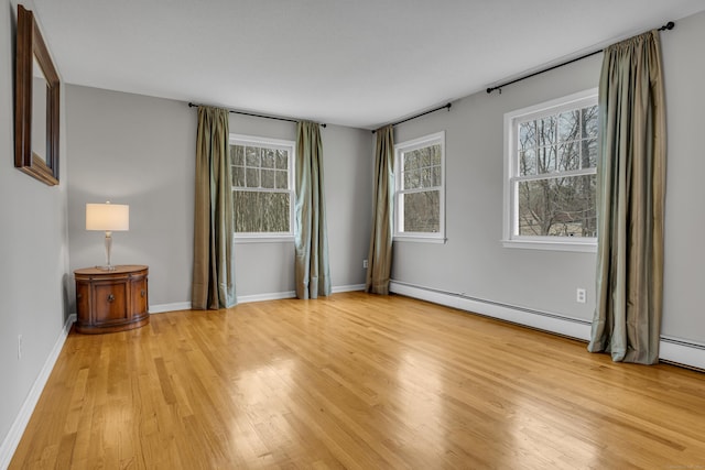 unfurnished room with a baseboard heating unit, light wood-style flooring, baseboards, and a healthy amount of sunlight