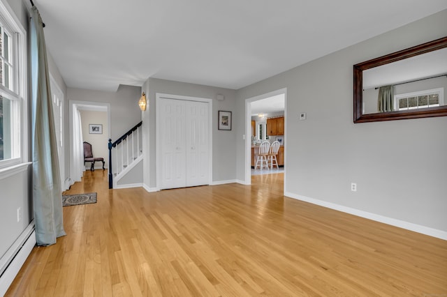 unfurnished living room featuring a baseboard heating unit, baseboards, light wood-style floors, and stairs
