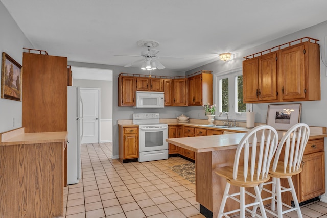 kitchen with a ceiling fan, a sink, white appliances, light countertops, and a peninsula