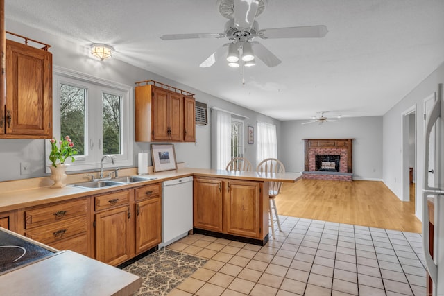 kitchen featuring a sink, dishwasher, ceiling fan, a fireplace, and a peninsula