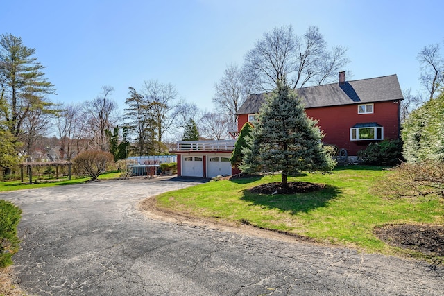 view of front of house featuring a chimney, driveway, a garage, and a front yard