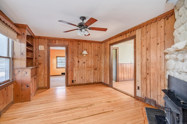 unfurnished living room featuring wood walls, a wood stove, visible vents, light wood-style floors, and ceiling fan