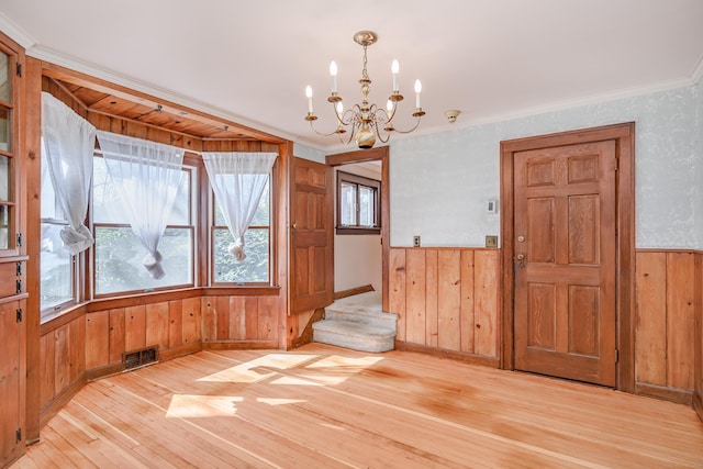 empty room featuring light wood finished floors, wood walls, a chandelier, and visible vents
