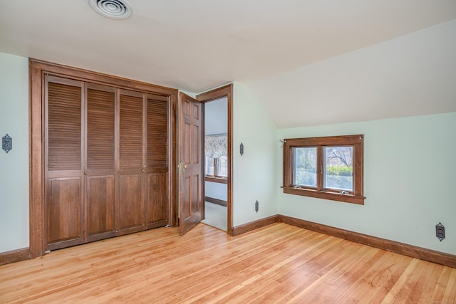 unfurnished bedroom with vaulted ceiling, light wood-type flooring, visible vents, and baseboards