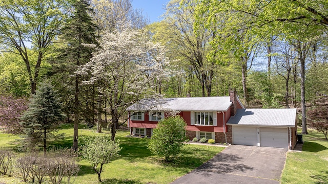 split foyer home featuring an attached garage, brick siding, a front yard, a chimney, and driveway