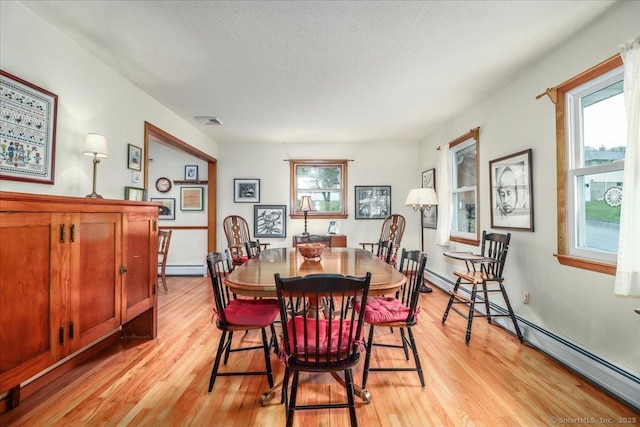 dining area featuring light wood finished floors, a baseboard heating unit, a baseboard radiator, and a textured ceiling
