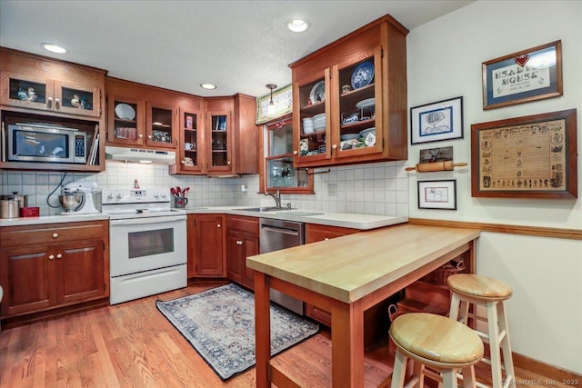 kitchen featuring stainless steel appliances, under cabinet range hood, a sink, backsplash, and light wood-style floors