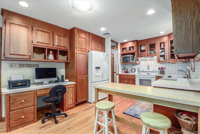 kitchen featuring white appliances, a sink, under cabinet range hood, light countertops, and light wood-style flooring