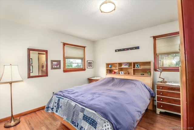 bedroom featuring wood finished floors, baseboards, and a baseboard radiator