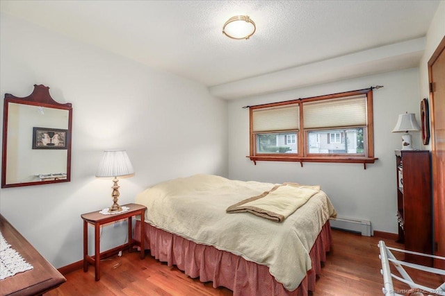 bedroom featuring wood finished floors, baseboard heating, baseboards, and a textured ceiling
