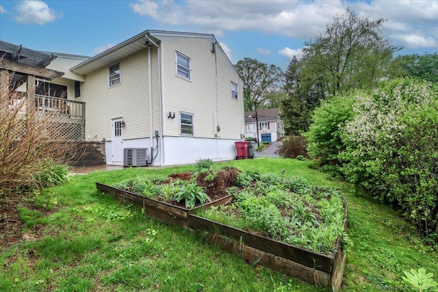 rear view of property featuring a vegetable garden, central air condition unit, and a lawn