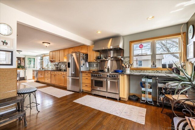 kitchen with plenty of natural light, dark wood finished floors, wall chimney exhaust hood, high end appliances, and backsplash