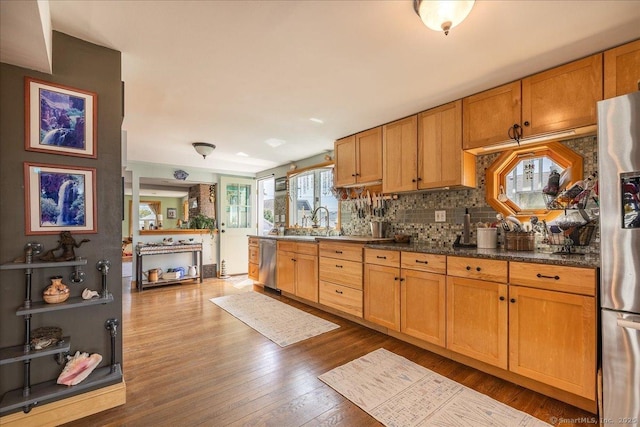 kitchen featuring a sink, dark wood-style flooring, stainless steel appliances, backsplash, and dark countertops