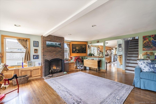 living area featuring beam ceiling, stairway, wood-type flooring, and a brick fireplace