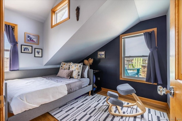 bedroom with baseboards, wood finished floors, multiple windows, and lofted ceiling