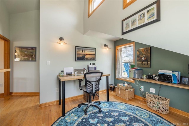 office area featuring plenty of natural light, baseboards, a towering ceiling, and light wood-style floors