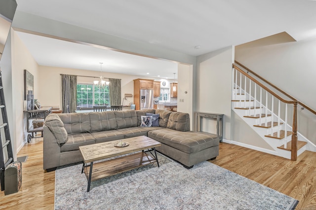living area featuring light wood-type flooring, stairway, a chandelier, and baseboards