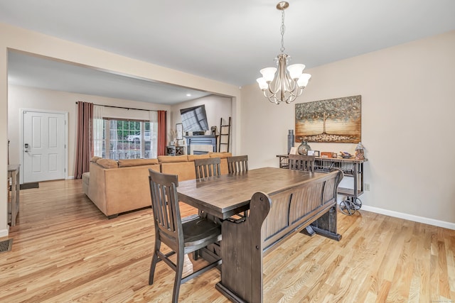 dining space featuring a chandelier, light wood-style floors, baseboards, and a fireplace