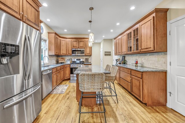kitchen featuring stainless steel appliances, a sink, stone counters, brown cabinetry, and recessed lighting