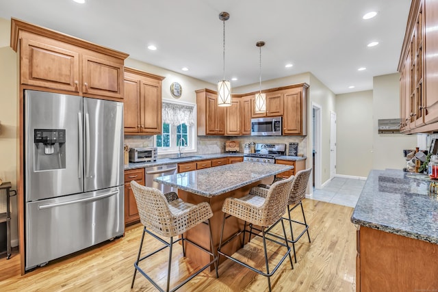 kitchen with stainless steel appliances, a sink, brown cabinets, a breakfast bar area, and backsplash