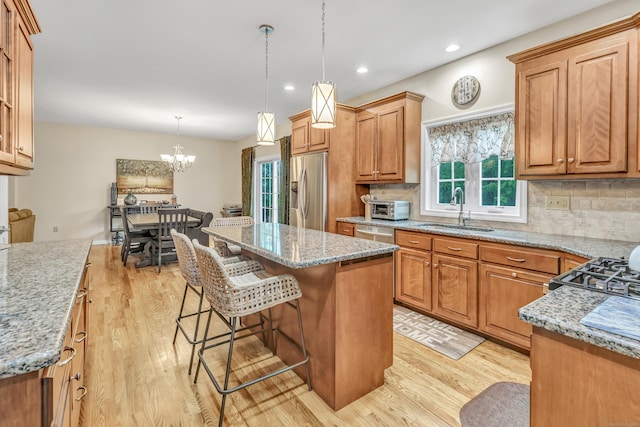 kitchen featuring a sink, appliances with stainless steel finishes, light wood finished floors, light stone counters, and recessed lighting