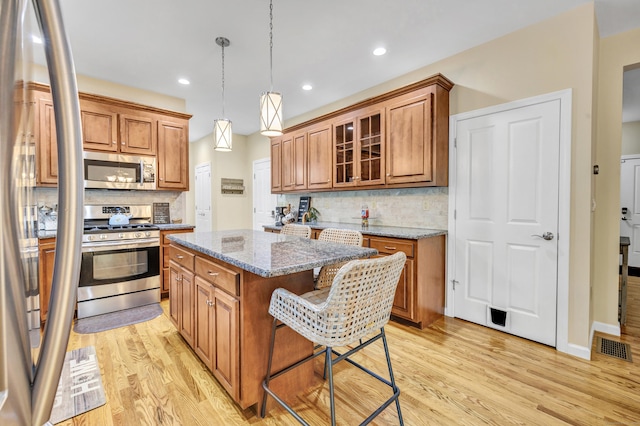 kitchen featuring appliances with stainless steel finishes, brown cabinetry, a kitchen island, light wood-type flooring, and recessed lighting