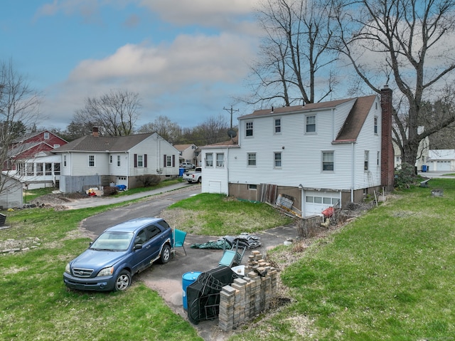 back of property featuring a residential view, driveway, a chimney, a garage, and a yard