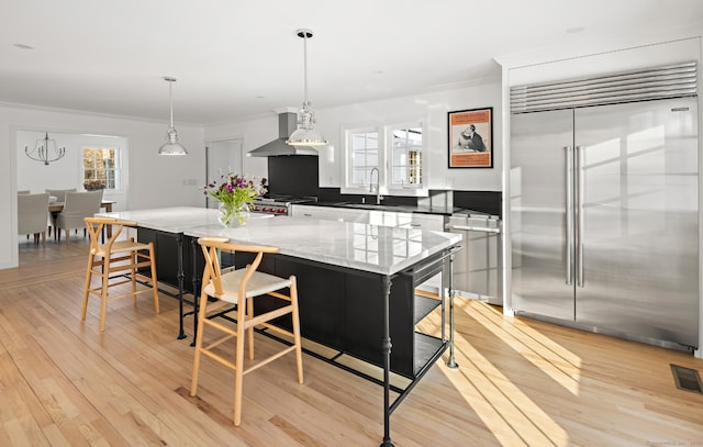 kitchen with stove, light wood-type flooring, crown molding, built in fridge, and wall chimney range hood