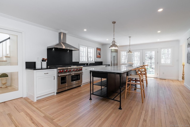 kitchen with wall chimney range hood, double oven range, crown molding, light wood finished floors, and french doors