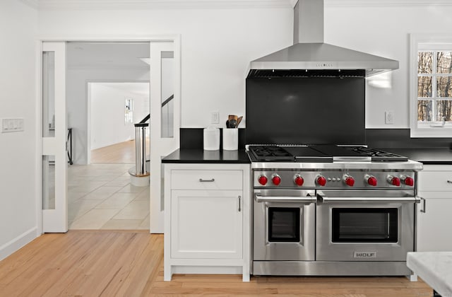 kitchen featuring crown molding, white cabinets, dark countertops, range with two ovens, and wall chimney exhaust hood