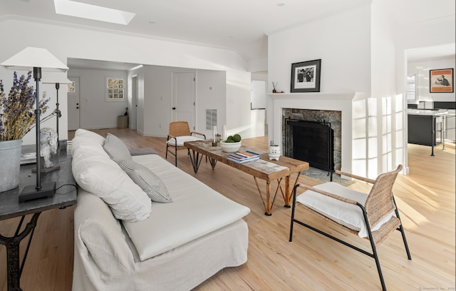 living area featuring light wood-type flooring, a stone fireplace, visible vents, baseboards, and a skylight