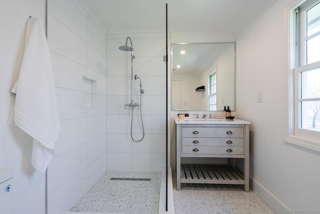 bathroom with a tile shower, a healthy amount of sunlight, speckled floor, ornamental molding, and vanity