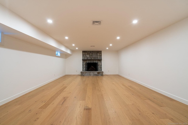 unfurnished living room with visible vents, light wood finished floors, a stone fireplace, and baseboards